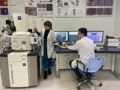 Polina Medvedskaya stands next to a scanning-electron microscope while Ivan Lyatun looks at the images on a computer monitor