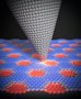 Illustration representing the friction between the tip of an atomic force microscope and graphene "Moiré" superstructures. The tip looks like a grey cone and the superstructures are represented by red hexagonal areas on a blue background
